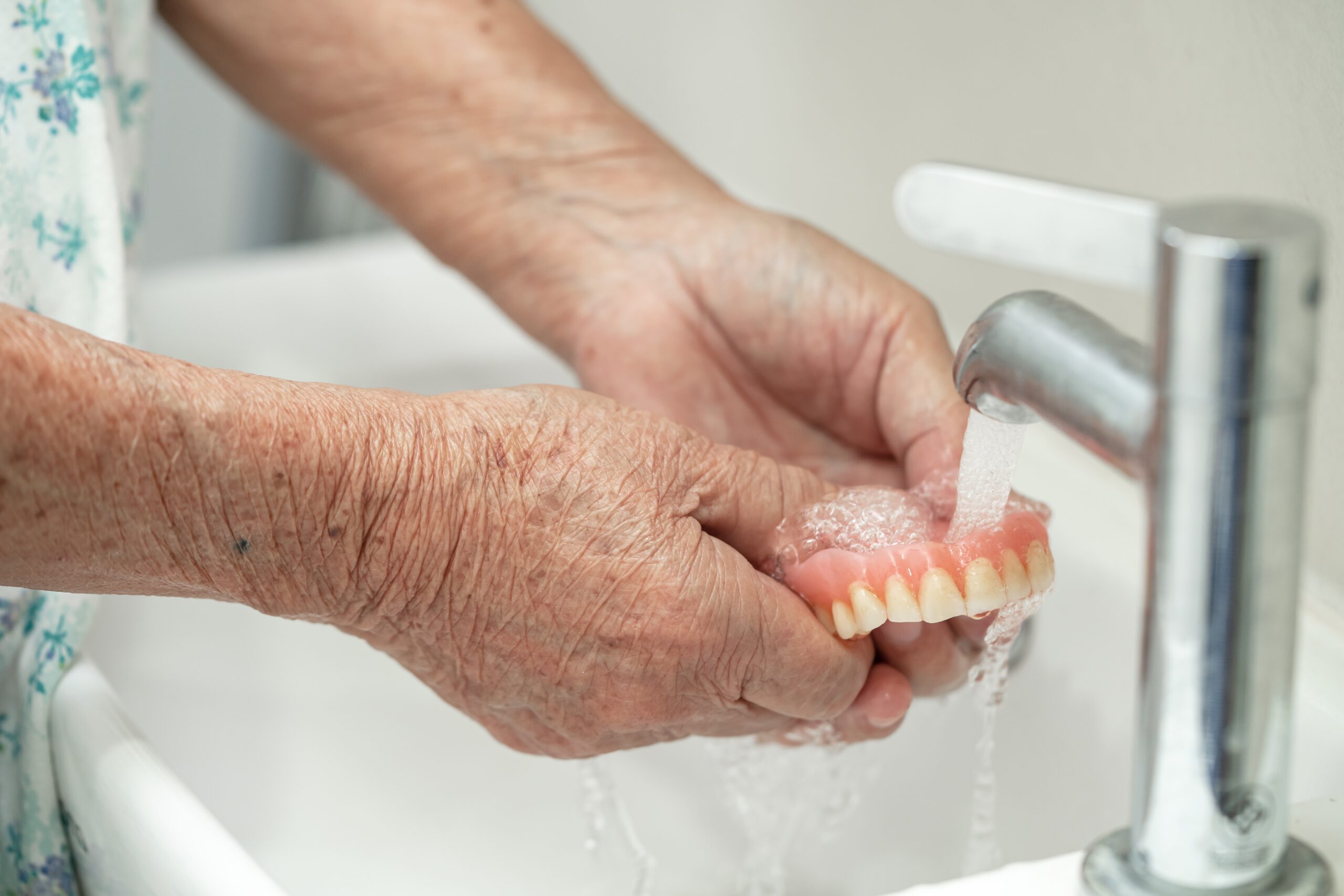 Senior adult cleaning dentures under running water